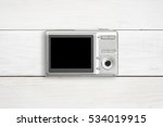 silver digital compact camera with blank black screen display place on center white vintage wood table and top view with copyspace