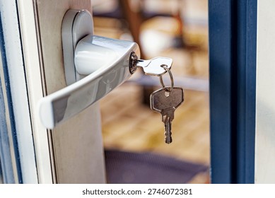 A silver door handle with keys inserted in the lock on a partially open door, showing a blurred indoor background with warm tones.