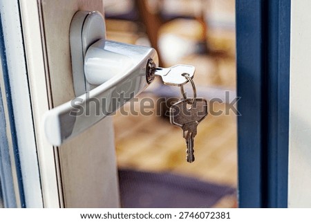 A silver door handle with keys inserted in the lock on a partially open door, showing a blurred indoor background with warm tones.