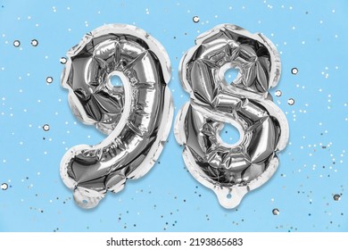 Silver Foil Balloon Number, Digit Ninety Eight On A Blue Background With Sequins. Birthday Greeting Card With Inscription 98. Top View. Numerical Digit. Celebration Event, Template.