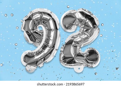 Silver Foil Balloon Number, Digit Ninety Two On A Blue Background With Sequins. Birthday Greeting Card With Inscription 92. Top View. Numerical Digit. Celebration Event, Template.