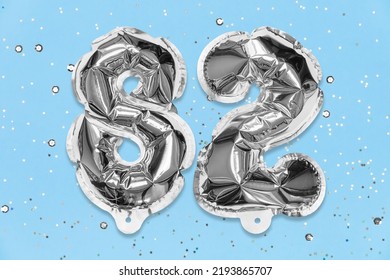 Silver Foil Balloon Number, Digit Eighty Two On A Blue Background With Sequins. Birthday Greeting Card With Inscription 82. Top View. Numerical Digit. Celebration Event, Template.