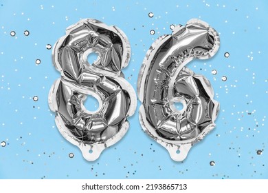 Silver Foil Balloon Number, Digit Eighty Six On A Blue Background With Sequins. Birthday Greeting Card With Inscription 86. Top View. Numerical Digit. Celebration Event, Template.