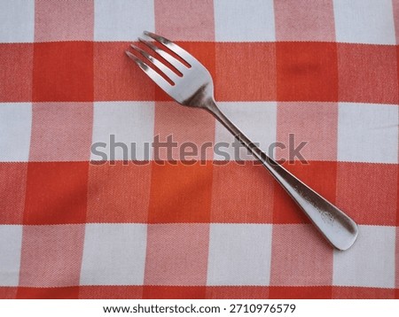 A silver fork put on the red and white checkered pattern tablecloth