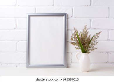 Silver frame mockup with meadow grass and green leaves in pitcher vase near painted brick wall. Empty frame mock up for presentation artwork. Template framing for modern art. - Shutterstock ID 695587015