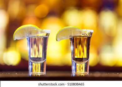 Silver And Gold Tequila In A Glass On A Background Of Bright Lights. Traditional Mexican Drink.