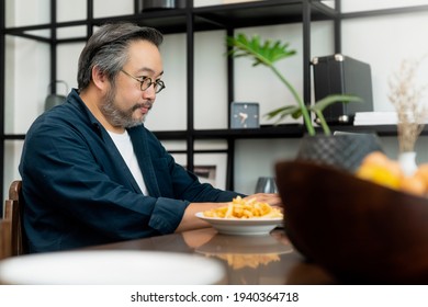 Silver Hair And Beard Male Dad Businessman Freelancer Working At Home Behind A Laptop With Super Busy Communication Smarthphone Calling. Remote Work And Family.