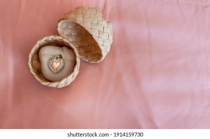 A silver heart-shaped locket on a small white pillow in a woven palm ring box on a pink silk pillowcase, London, Ontario, Canada.
