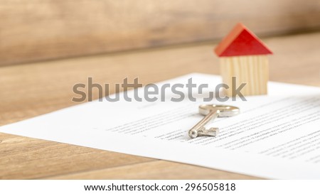 Silver house key lying on a contract of house sale, lease, insurance or mortgage in a real estate concept, viewed low angle with focus to the tip.