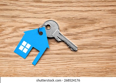 Silver key with blue house figure on wooden background