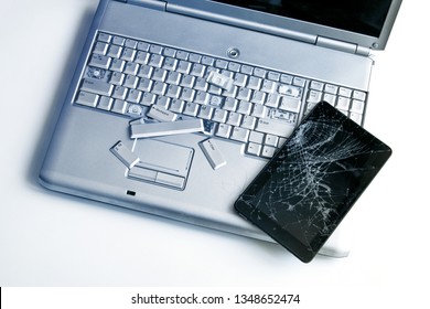 A silver laptop with a broken keyboard and a tablet with a cracked display. A close-up picture of part of broken laptop and cracked screen on a tablet.
