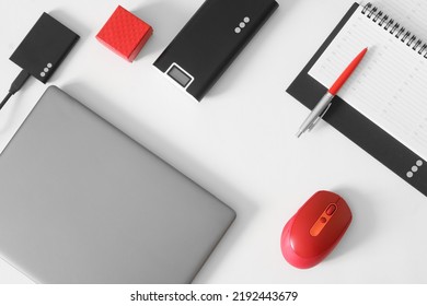 Silver laptop, computer mouse, pen, planner, portable ssd, power bank and red box on white background. Concept of a modern workplace, business planning and digital data preservation. Close-up