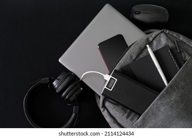 Silver laptop and modern gadgets lie in a gray backpack on a dark table. Travel, trip, study and lifestyle with modern computer technology. Close-up - Shutterstock ID 2114124434