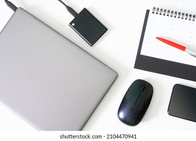 Silver laptop or ultrabook, computer mouse, pen, diary, portable ssd and smartphone on a white background. Concept of workplace, business planning and digital preservation. Close-up