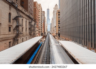 Silver light train pulling away from an elevated station in downtown Chicago on a cloudy spring day