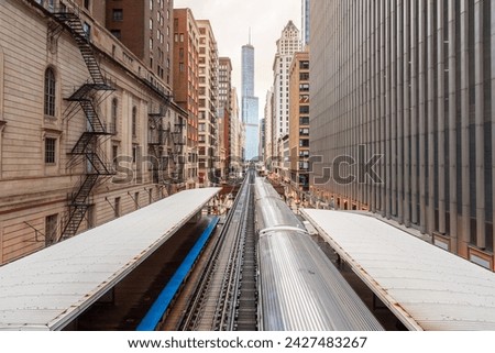 Silver light train pulling away from an elevated station in downtown Chicago on a cloudy spring day