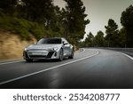 Silver luxury sports car speeding through a winding forest road, showcasing agility and performance. Front view captured during a dynamic drive at dusk.