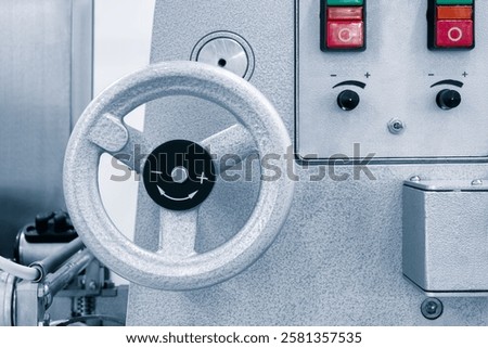 A silver machine with a silver wheel and a red button. The wheel is black and has a smiley face on it