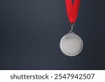 Silver medal with red ribbon on dark grey background, space for text