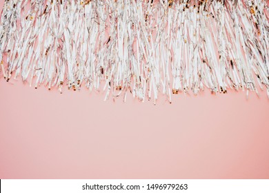 Silver metal foil tinsel strips isolated on pink background, christmas or festive decoration garland. Pom-poms cheerleading. New year composition. Flat lay,  copy space. Sparling decorative element.