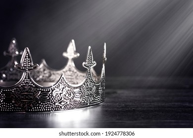 A Silver Metal King Or Queens Crown On A Black Wood Table