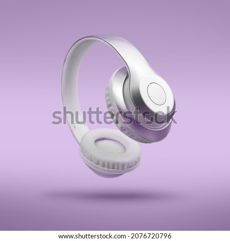 Silver metallic white wireless headphones in the air on Lavendula purple background. Trendy minimal music device flying levitation concept of accessories. New technologies. Closeup high resolution