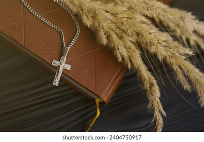 Silver necklace with crucifix cross on christian holy bible book on black wooden table. Asking blessings from God with the power of holiness, which brings luck - Powered by Shutterstock