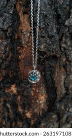 Silver necklace jewelry in the shape of a crescent moon decorated with bright blue stones in the middle with a wood texture background