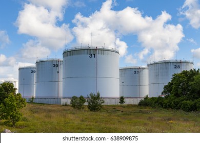 Silver Oil Tanks On The Green Grass Field. Blue Sky With Clouds.