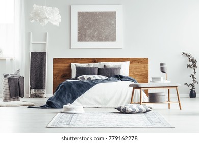 Zilveren schilderij op witte muur boven bed in designer slaapkamer interieur met ladder, lampen en lakens