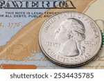 A silver quarter dollar coin sits on top of a United States of America bill. The coin is from the year 1976