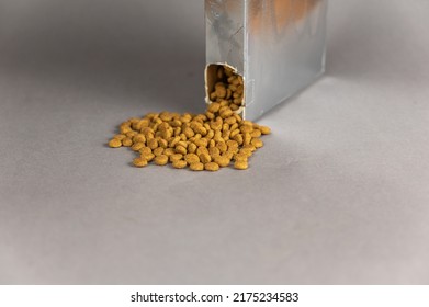 A Silver Rectangular Box Against A Gray Background. Pet Food Spilling Out Of The Hole. Dry Pelleted Food. Pet Food. Selective Focus.