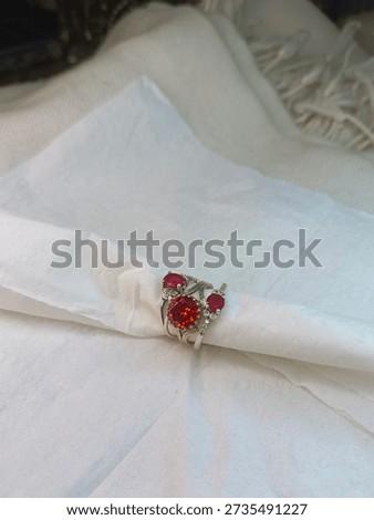 A silver ring adorned with a cluster of red gemstones, resting on white fabric.