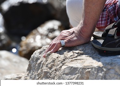 A silver ring with a cross and diamonds on the finger of an elder man who sits on a coastal rock. - Powered by Shutterstock