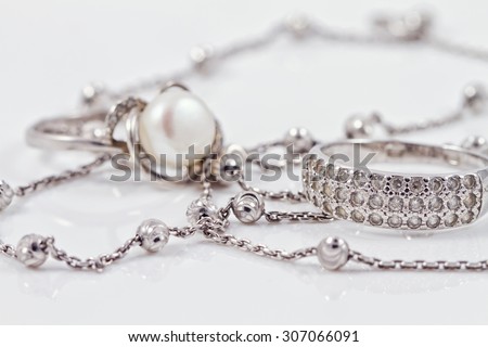 Silver ring with precious stones and pearl are together with a silver chain on acrylic
