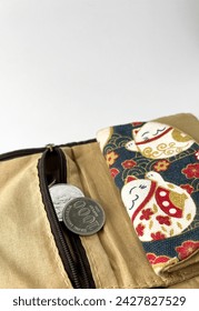 Silver rupiah coin money coming out from wallet zipper with dark blue and light brown fabric material and japanese neko cat design object isolated on white studio background.