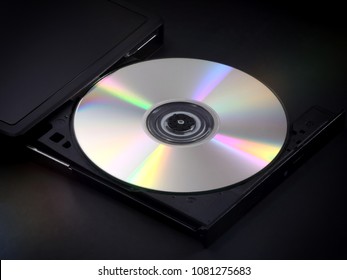 A silver, shiny CD is shown ejected in the tray of a portable multimedia disc player.