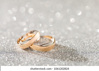 Silver sparkling glitter bokeh background with golden wedding rings. Shallow focus. Copy space