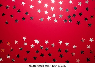 Silver Star Sprinkles On Red Backgound. Festive Holiday Confetti. Celebration Concept. Top View, Flat Lay.