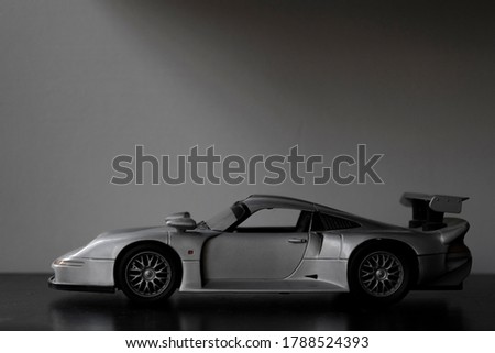 silver supercar toy on black table. Wall in the background. 