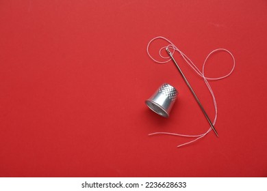 Silver thimble, needle and thread on red background, flat lay. Space for text