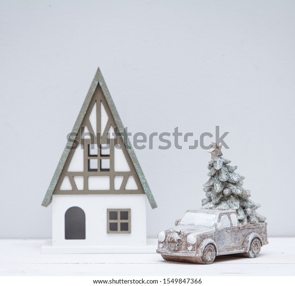 A silver toy retro car stands with a Christmas\
tree near a beautiful toy house. Christmas retro composition on\
light background. Place for\
text.