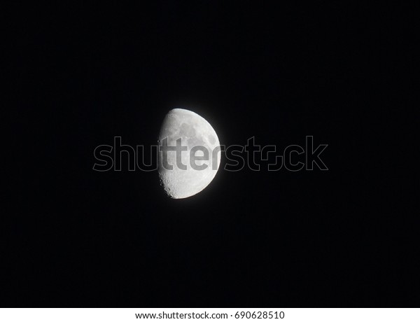 silver two thirds bright moon in a black sky\
showing seas and craters in shadow \
