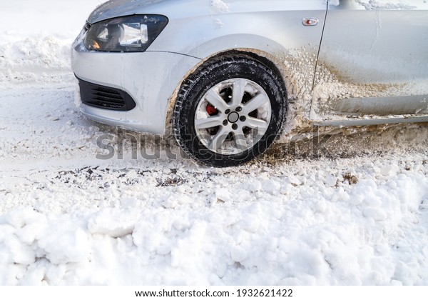 Silver vehicle moving on snowy road skidding,\
car\'s wheel spin and throw out pieces of snow it attempts to gain\
traction on the slippery\
surface.