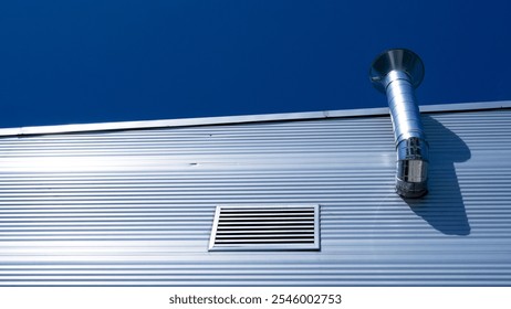 Silver ventilation duct against a blue sky on building roof - Powered by Shutterstock