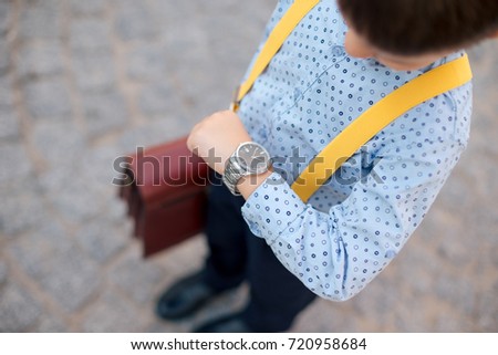 Silver watch on the hand of future businessman in blue shirt, with brifcase and yellow suspenders. Time on wrist watch. Man with clock checks the time. Hand with clock.