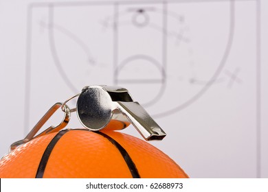 A silver whistle laying on an orange basketball in front of the game plan. - Powered by Shutterstock