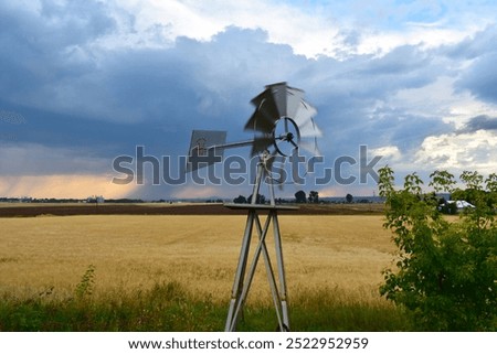 Silver Windmill Spinning in front of a Field and Rain Clouds
