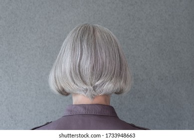 Silver-haired mature lady on gray background, from behind.