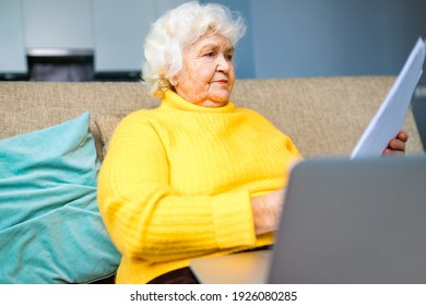silver-haired mature russian unhappy woman holding at banking paper bill in living room at modern house